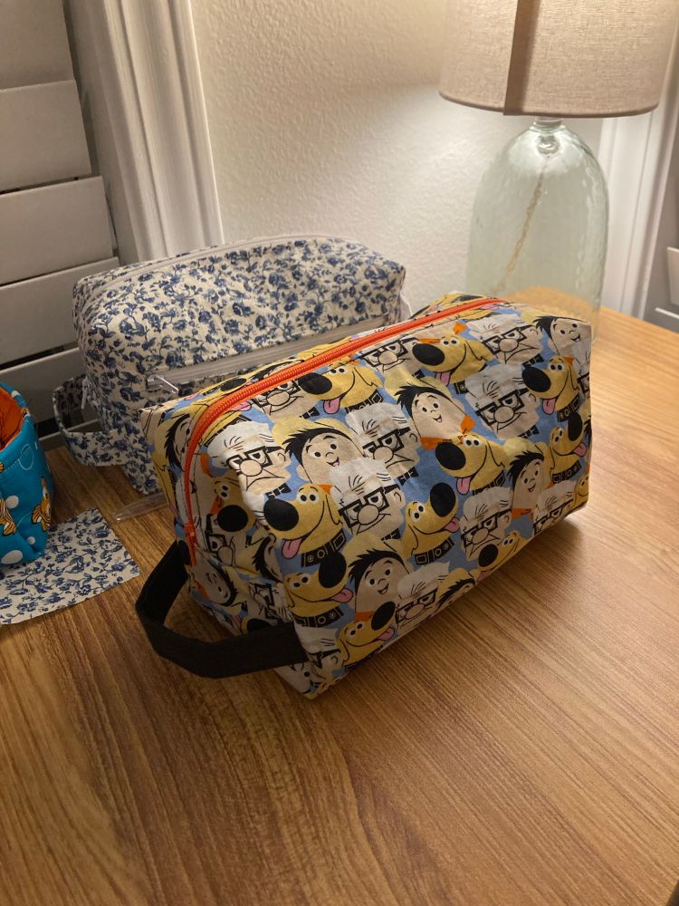 Two cosmetic bags sitting on a table. One is a pattern from Disney’s “Up” and the other is blue floral. 