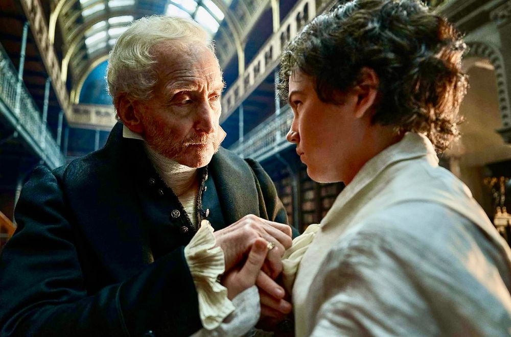 Charles Dance faces a boy in a wide high ceiling hallway with glass ceilings