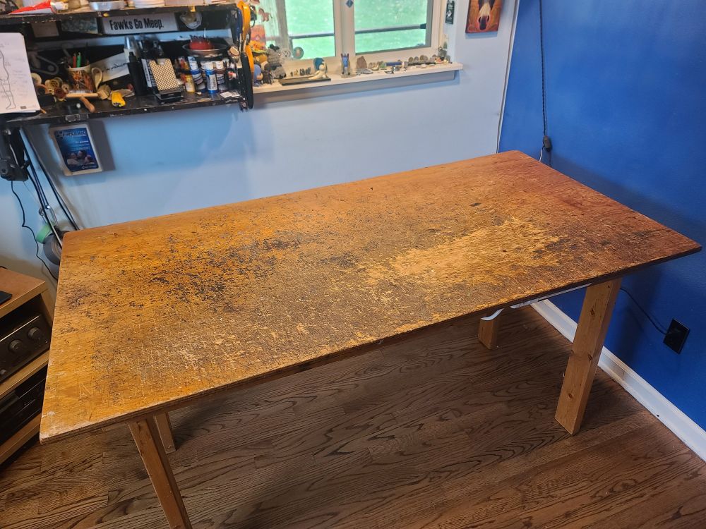 A wooden worktable, the surface covered in cuts and a patch missing where a lot of work has been done.