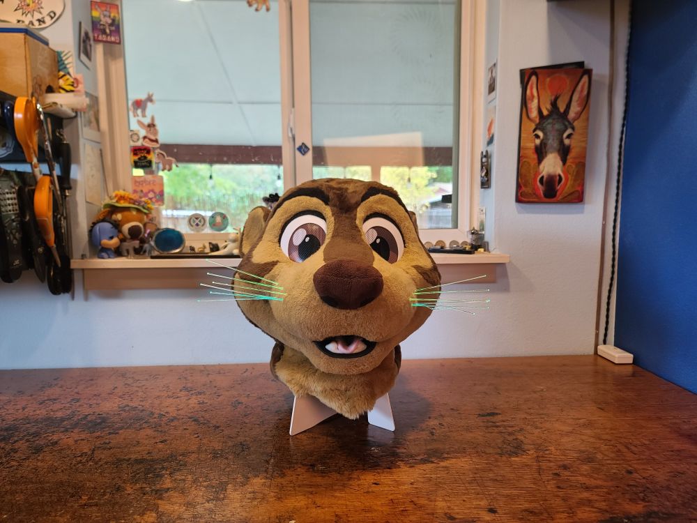 Otter fursuit head with a happy expression without eyelids attached and glowing whiskers