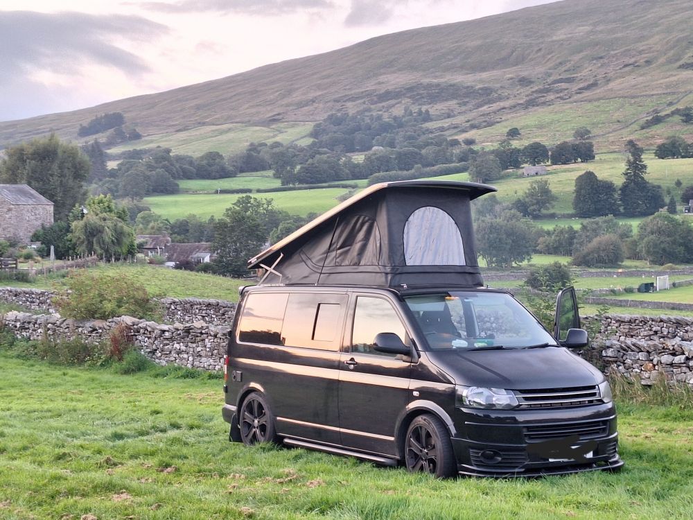 Very cool black campervan named Geoff, parked in a field with the top.popped.