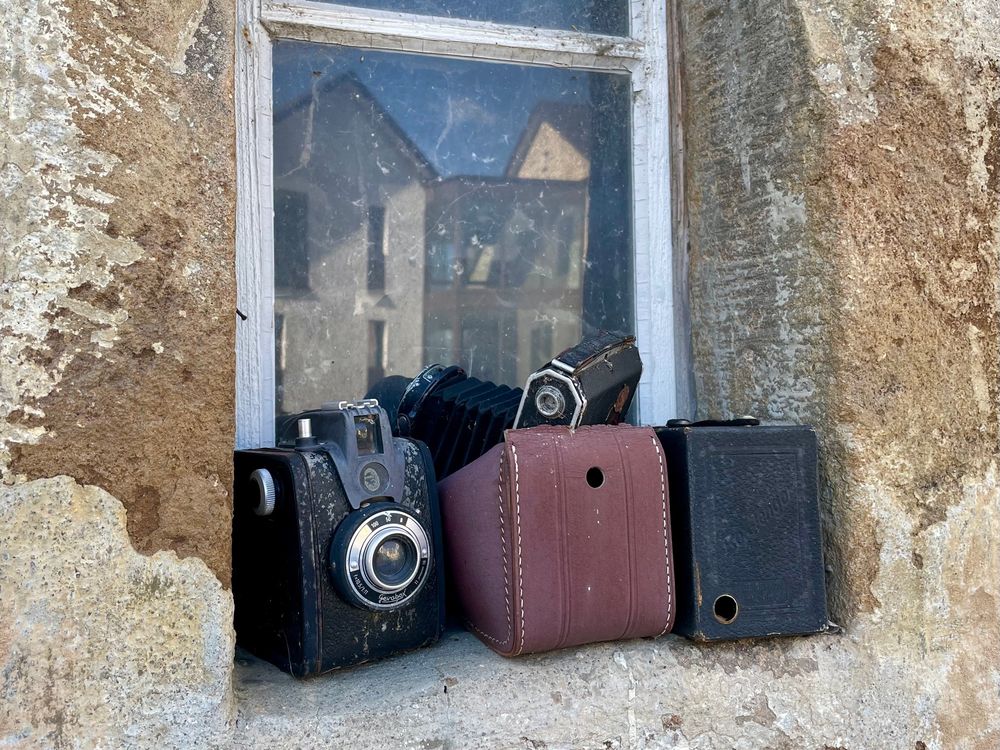 Ein Teil eines alten Fensters. Auf der Fensterbank liegen drei alte Kameras.