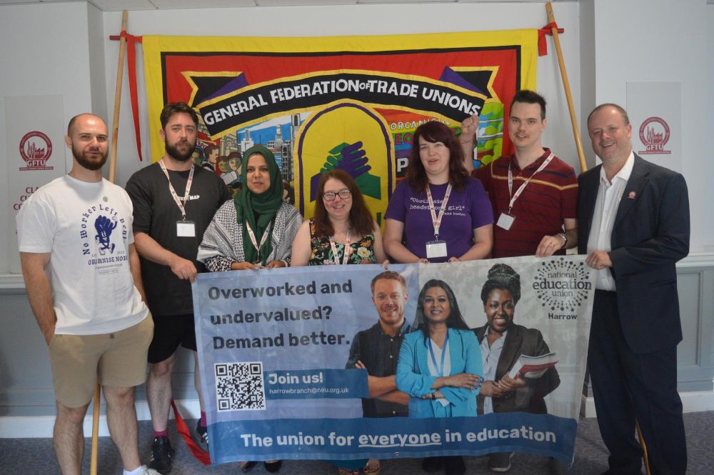 Group of eight individuals standing behind a banner for the General Federation of Trade Unions, displaying advocacy messages such as "overworked and undervalued? Demand better."