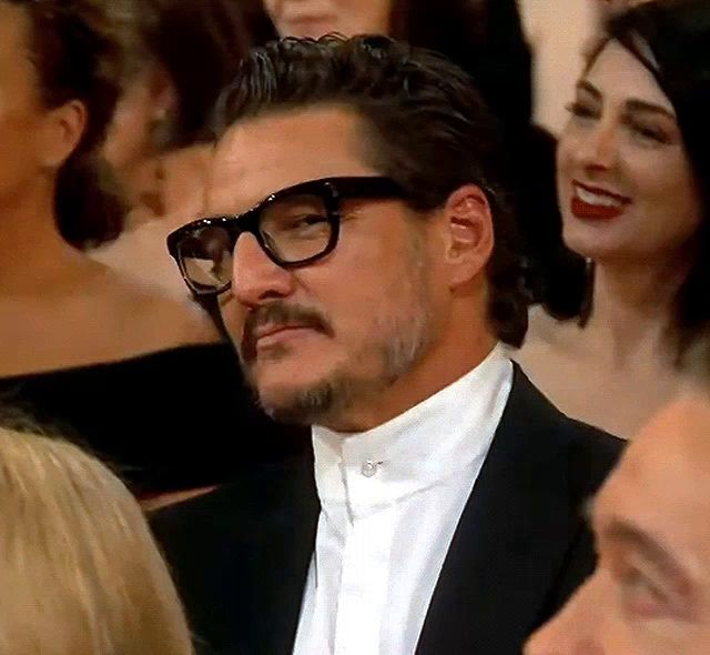 a man wearing glasses and a tuxedo is sitting in a crowd