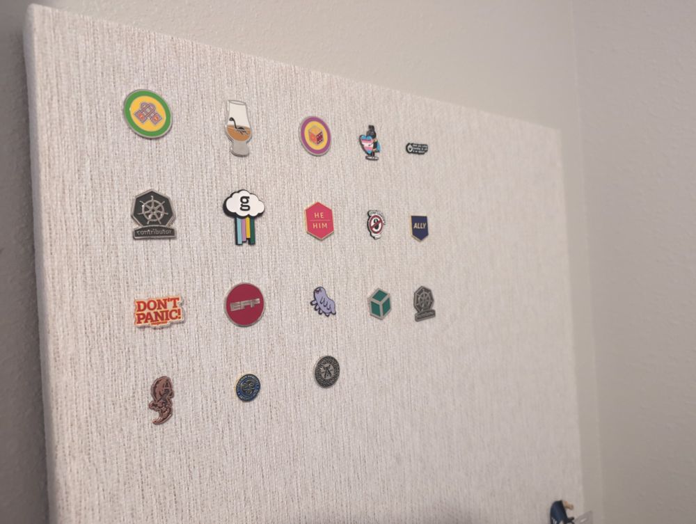 A corkboard with 18 pins hanging on a wakk