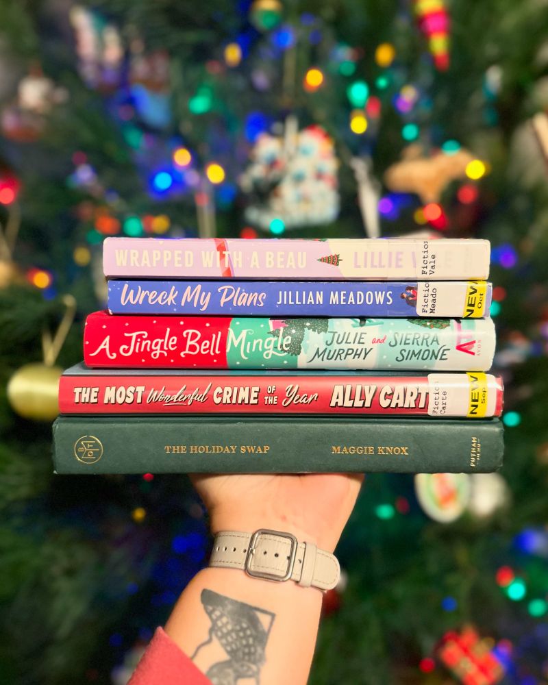 Book stack in front of a Christmas tree. Books are:
Wrapped With a Beau by Lillie Vale
Wreck My Plans by Jillian Matthews
A Jingle Bell Mingle by Julie Murphy and Sierra Simone
The Most Wonderful Crime of the Year by Ally Carter 
The Holiday Swap by Maggie Knox
