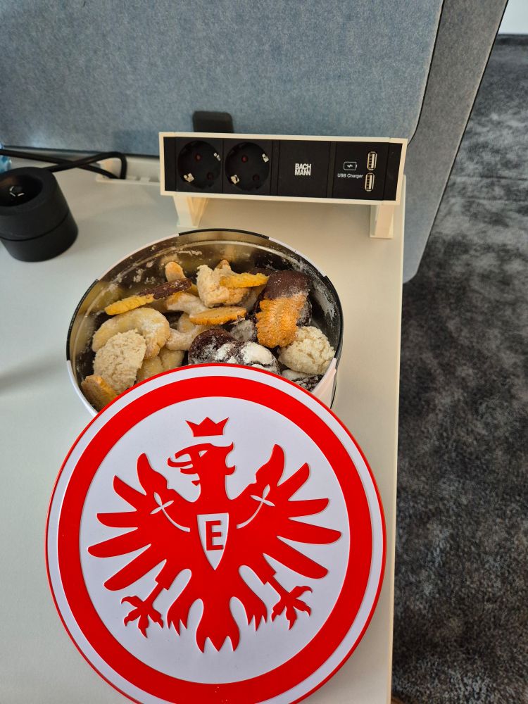 Eine Dose gefüllt mit Plätzchen (Spritzgebäck, Kokosmakronen, Vanillekipferl und Schoko-Plätzchen). Der Deckel der Dose liegt vor der Doye und zeigt den Eintracht Adler 