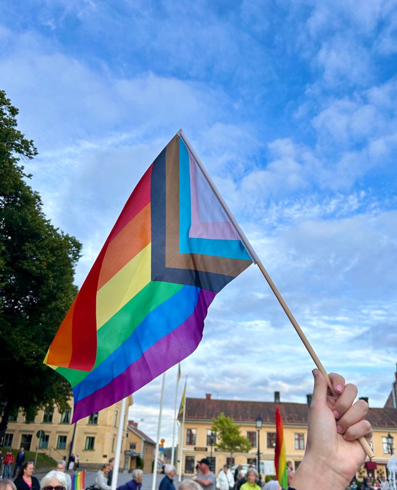 Progressive pride flag against a blue sky. 