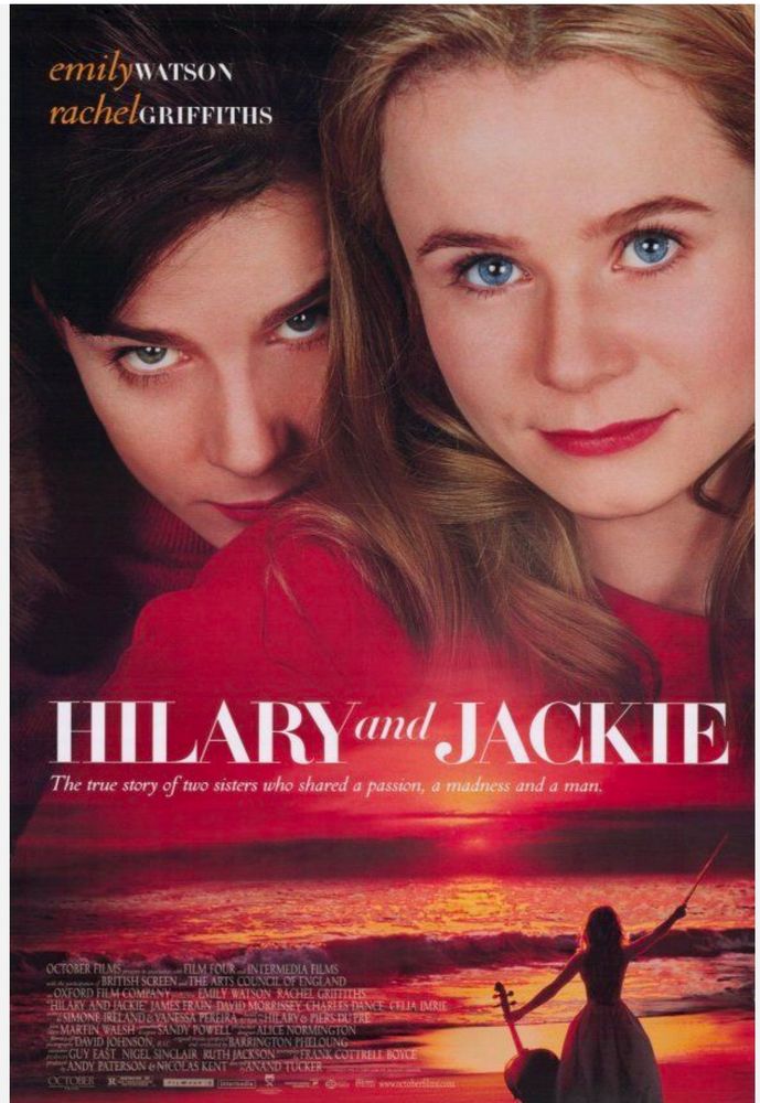 Hilary and Jackie: A close-up of two women, both wearing red top/dress. The woman in the foreground has dark-blonde hair, bright blue eyes, and a soft, confident expression. Behind her, another woman with dark hair and green eyes gazes directly at the viewer with a timid look. Below them, a woman in a long dress stands on a beach at sunset, holding a cello and bow. This poster represents the story of British classical musicians Jacqueline du Pré (cello) and Hilary du Pré (flute), played by Emily Watson and Rachel Griffiths. The tagline reads, “The true story of two sisters who shared a passion, a madness and a man.”
