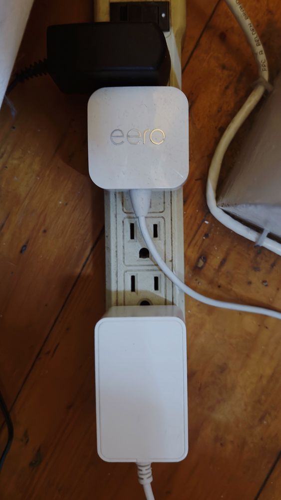 Power strip against a wooden floor with open sockets obscured by wire placement and large plug size