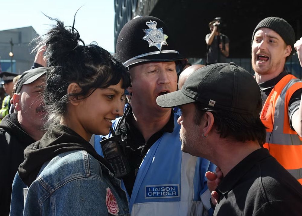 British Asian woman Saffiyah khan (left) dressed in a denim jacket over a black hoodie faces down english defence league (edl) protester wearing a black baseball cap with a defiant and mischievous grin on her face.