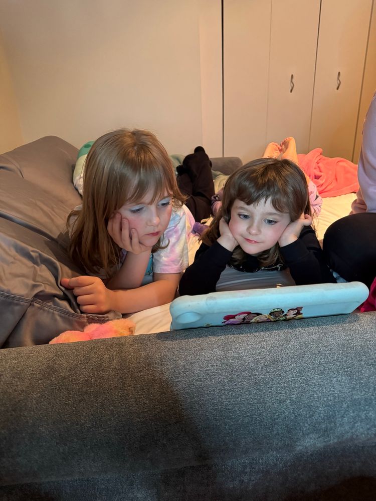 two young girls lying on a futon staring at a tablet 
