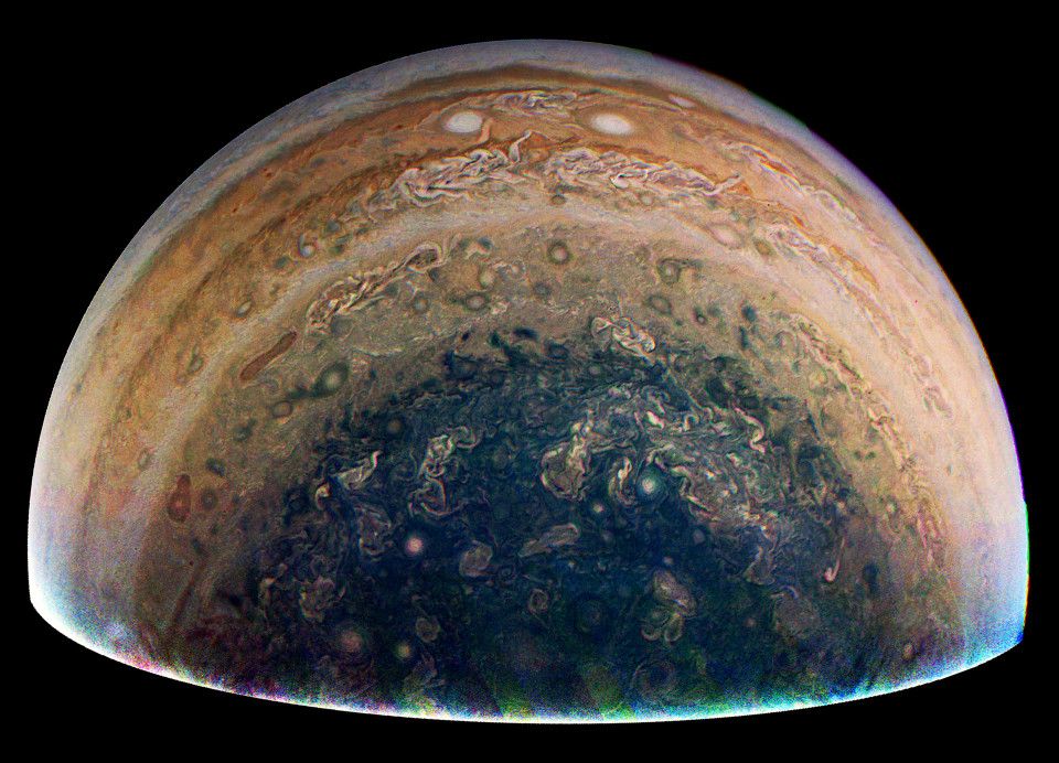 Wide view of Jupiter's southern latitudes, focusing on the area surrounding the pole. A few cloud bands are visible around the polar hood, and multiple turbulent storms are spread throughout the entire field of view.
