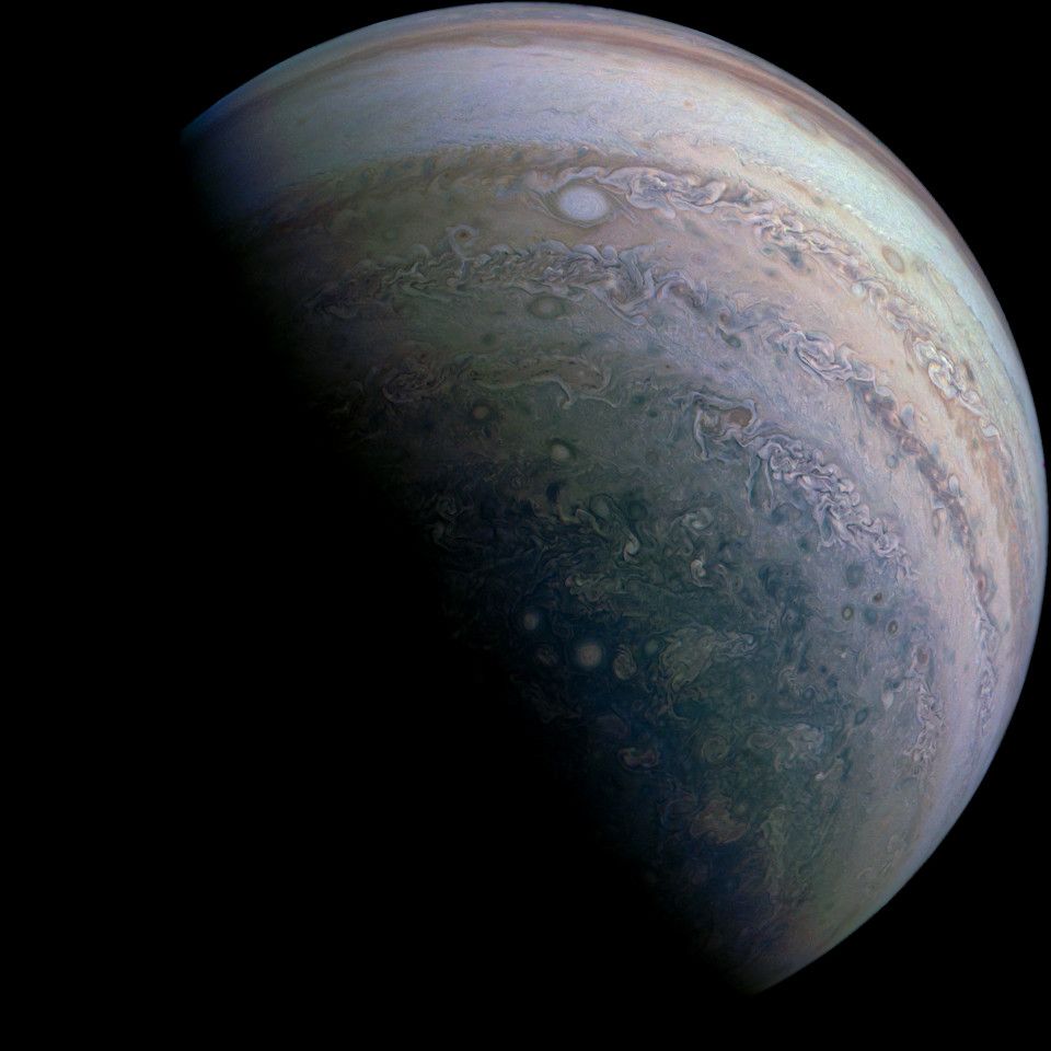 Photo taken above Jupiter's southern hemisphere. The south polar region is visible, with a distinct blue colouration, in contrast with paler brown/beige tones of the cloud bands seen in the rest of the planet's visible """surface""". Multiple turbulent and oval storms are seen.