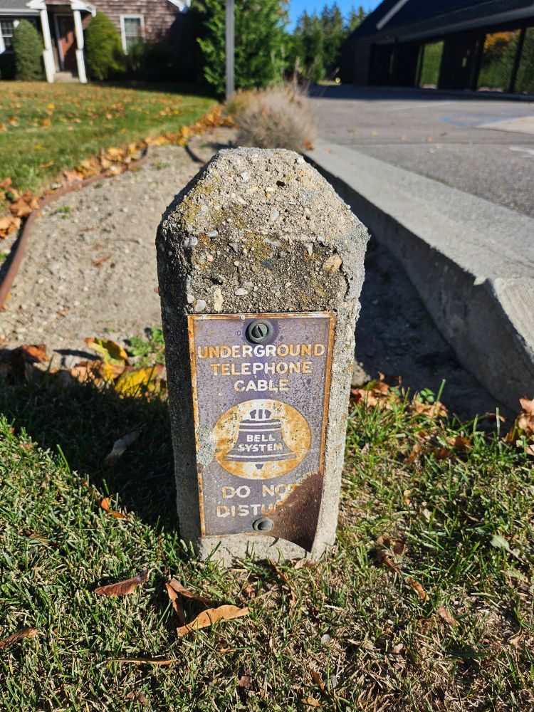 Small concrete pillar with a faded sign that says "Underground telephone cable" above the Bell System logo