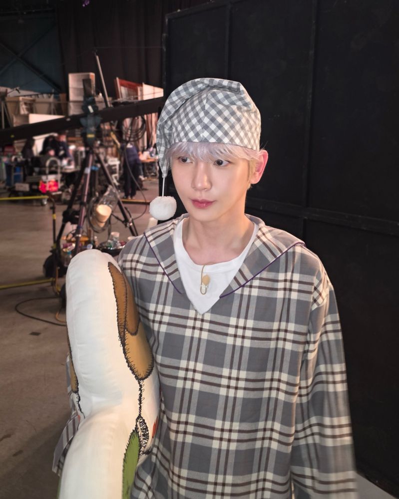 Key wearing a grey tartan nightshirt and matching cap with a white bobble on it, and holding a pillow