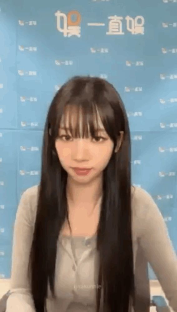 a young girl with long hair and bangs is standing in front of a blue wall .