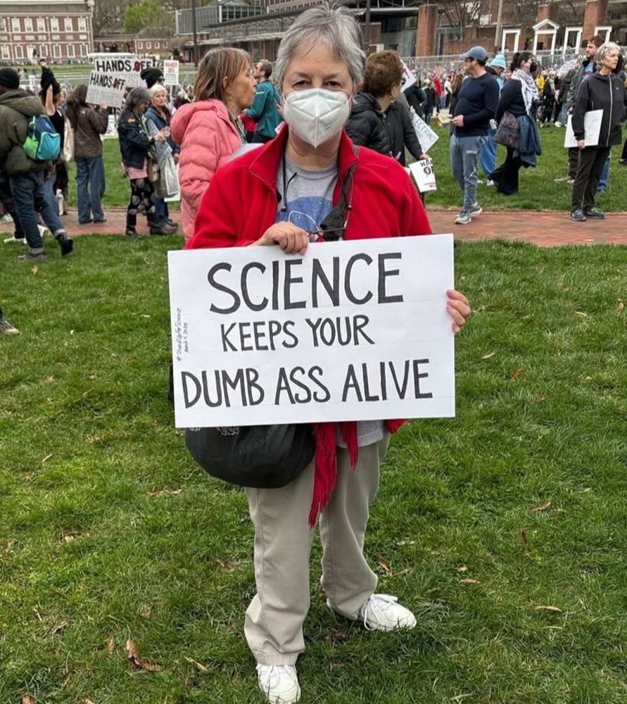 A person wearing a respirator and a sign that reads: Science keeps your dumb ass alive