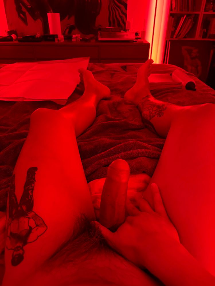 A POV pic: me from the waist down, laying on the bed, holding my cock. Pads and a lube bottle further away indicate a fisting scene.  