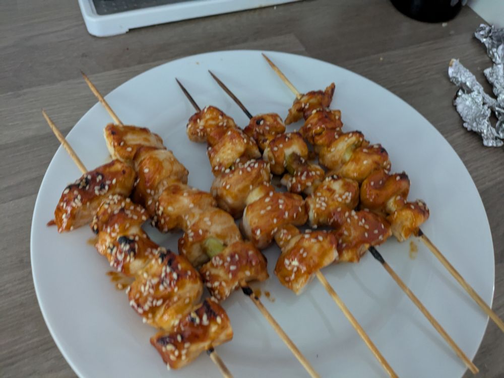 A plate of 5 chicken and spring onion skewers, coated in Korean BBQ sauce and sesame seeds