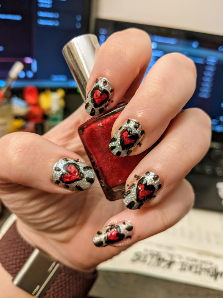 a nail design with red hearts and bold black lines, with a disco ball glimmer background. the person is holding the bottle of shimmering red polish.