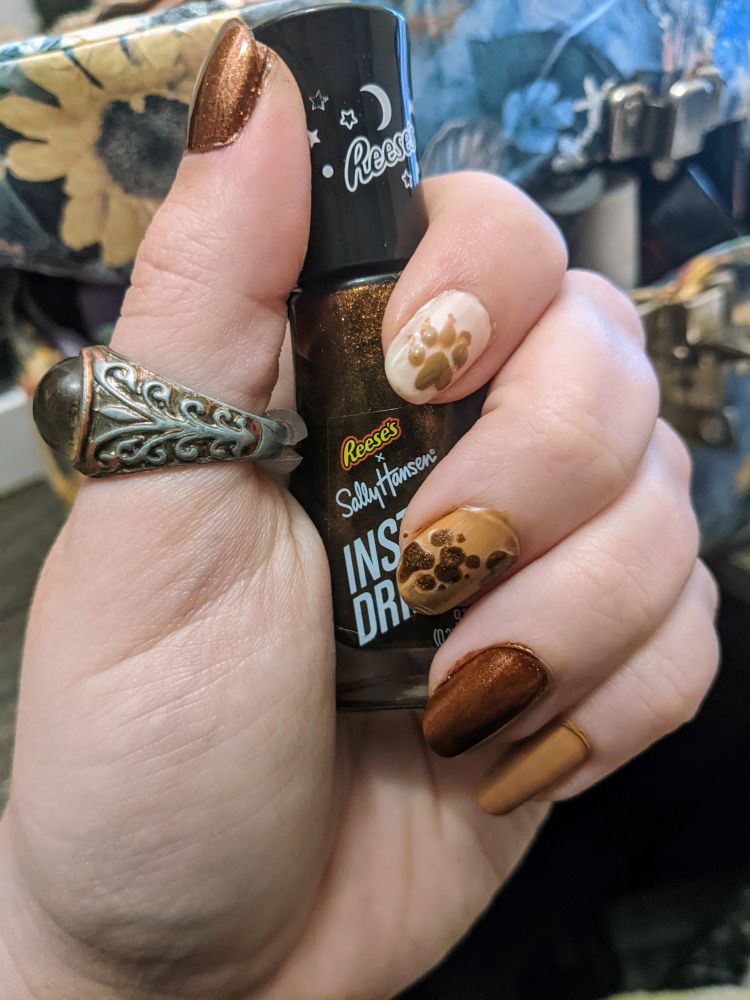 a nail design in a variety of browns with wolf pawprints on the nails. the person is holding the shimmering brown polish, which is a Reese's and Sally Hansen crossover.