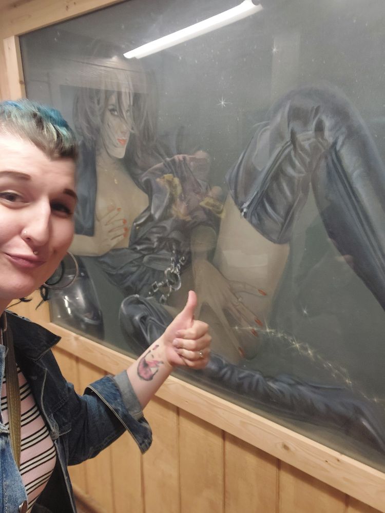 Harmony, six cocktails deeps, giving a thumbs up to the picture in the tavern bathroom where a woman in leather squirts glitter