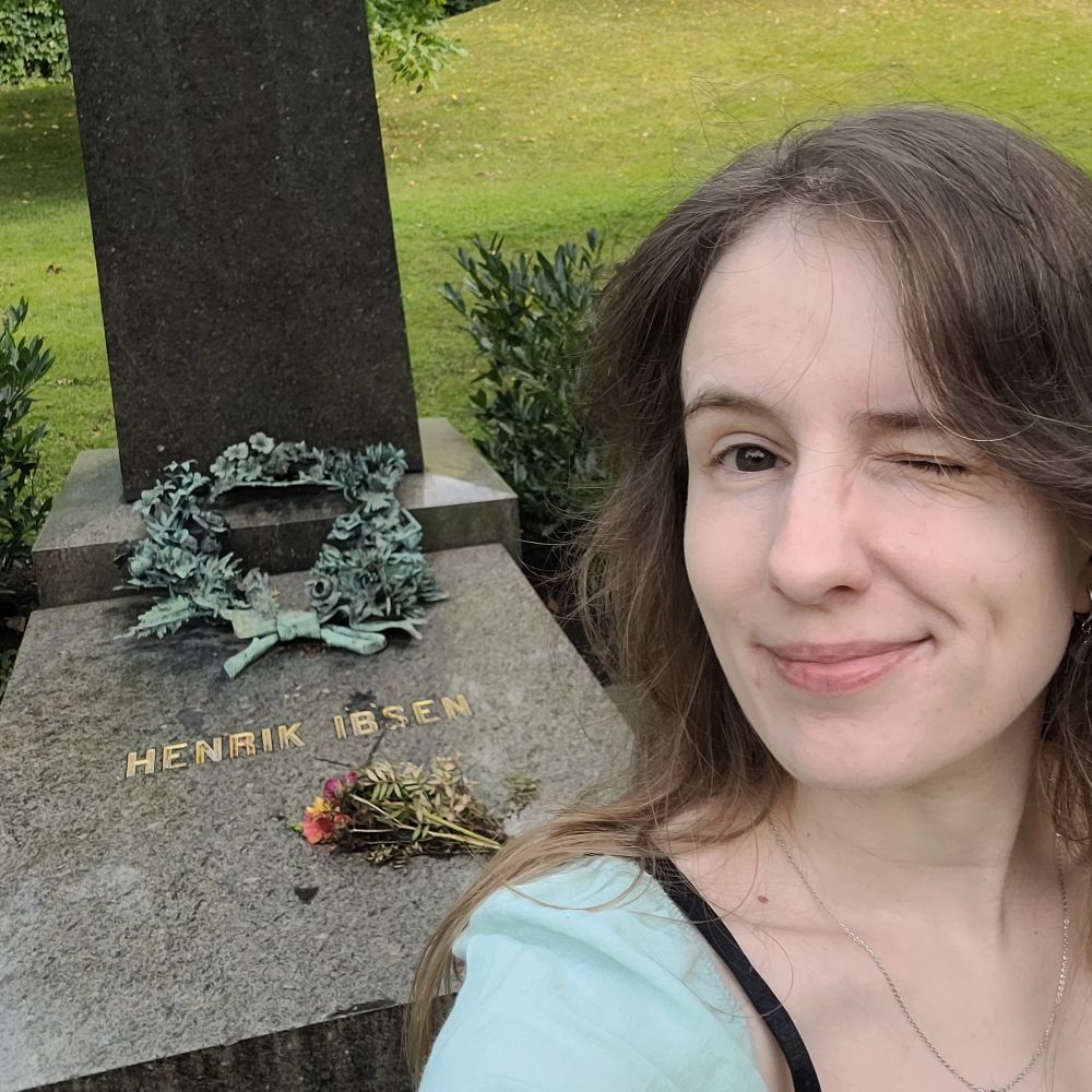 A woman winks in fron of Henrik Ibsen's grave.
