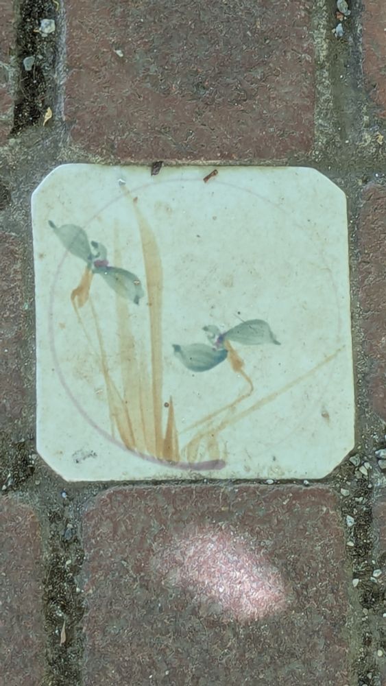 Painted tile inset into brick courtyard. Tile shows possibly an orchid. Photo by Ellen Friedman