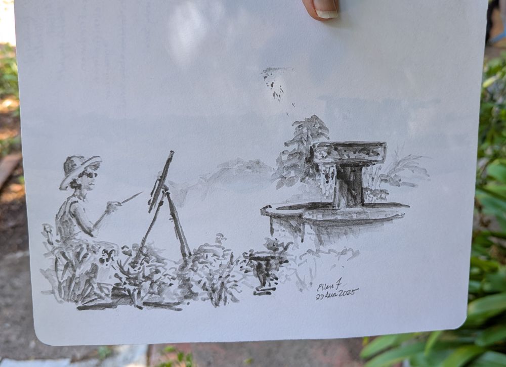 Quick sketch in shades of grey and black using soluble graphite and brush. Graphite is ArtGraf. Sketch is in a small sketchbook, done outdoors, showing a woman artist at the left, painting at an easel. Beyond her is a heavy pedestal-style fountain surrounded by low shrubs. Drawing by Ellen Friedman 30 Aug 2025.