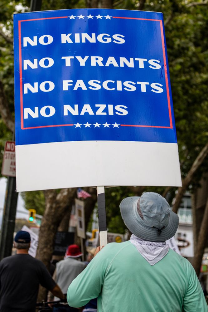Man in green shirt carrying blue sign with white lettering that reads "No Kings, No Tyrants, No Fascists, No Nazis" 
This is an anti-tRump takover protest in San Jose CA 16 Aug 2025. https://www.probonophoto.org/2025/FTTT/16Aug25SanJoseFightTrump/i-JhvqbKJ/A