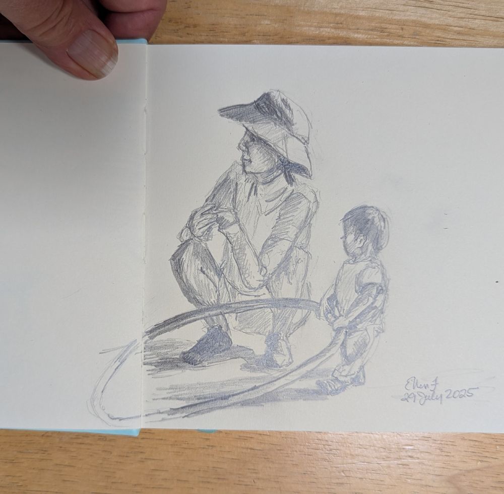 Graphite pencil sketch of young mother wearing a sun hat, crouched down next to a toddler. The toddler is standing and holding a large hulu-hoop with both hands. Sketch by Ellen Friedman