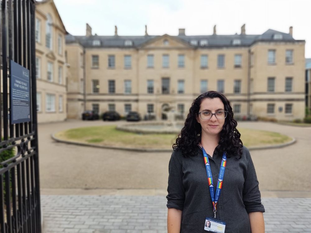 I'm standing against a backdrop of the Radcliffe Observatory Quarter, University of Oxford wearing a dark grey shirt and my new university lanyard. 