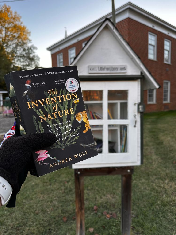 Hand holding a book in front of a free library. 