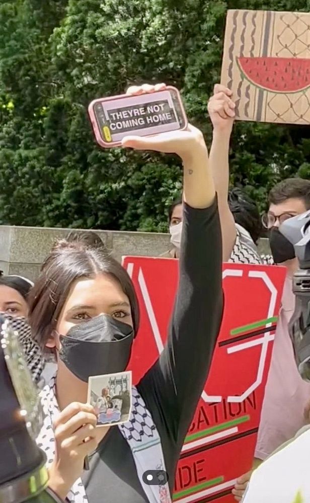 A masked pro-Palestinian protestor at the Israel Day parade today (June 2, 2024) in Manhattan holding up a her phone that has text on it reads “They’re Not Coming Home.”