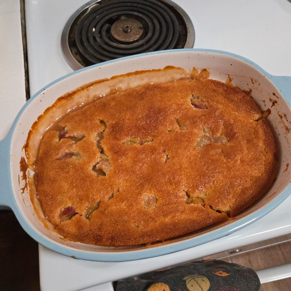 Peach cobbler in a casserole dish sitting on a stove.
