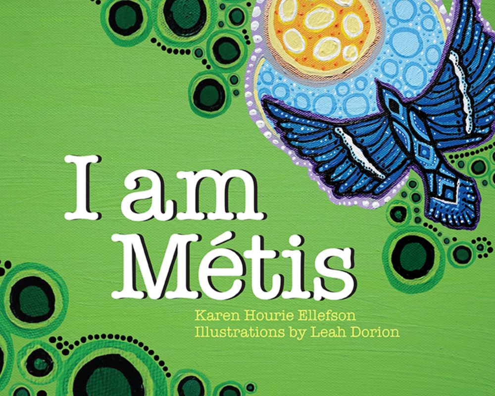 Book cover for I Am Metis by Karen Hourie Ellefson and illustrated by Leah Dorion (Fitzhenry & Whiteside Ltd) with a navy bird flying over a light blue circle suggestive of a lake, next to green circles suggestive of trees seen from above. "Who are you?", whispers the voice in the wind. "You are Métis." What does this strange word mean? A young girl watches her father to understand the unfamiliar label. Through a series of vignettes centred around her dad, the child interacts with her riverlot surroundings and delights in her Métis way of life. https://www.fitzhenry.ca/Detail/155455621X