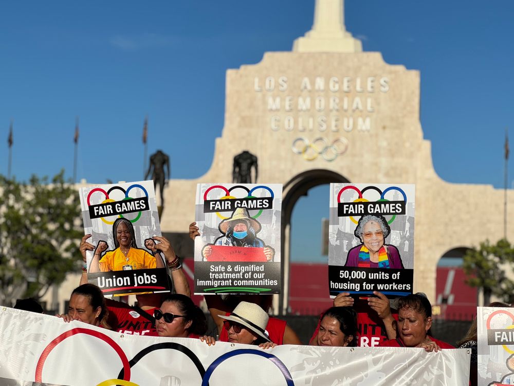 Signs in front of the LOS ANGELES MEMORIAL COLISEUM that read FAIR GAMES Union jobs FAIR GAMES Safe & dignified treatment of our immigrant communities FAIR GAMES 50,000 units of housing for workers 