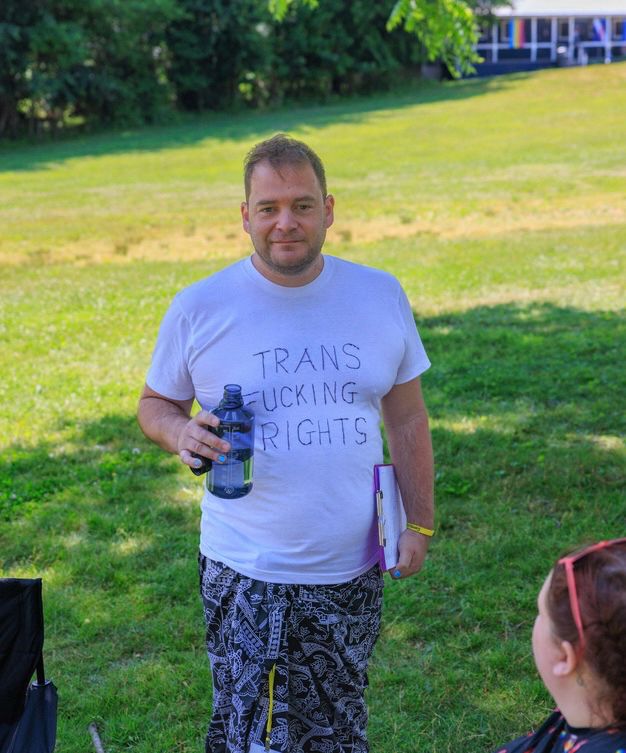 Yours truly at a festival, wearing a white t-shirt that I sharpied “TRANS FUCKING RIGHTS” on for extraordinarily necessary reasons last summer