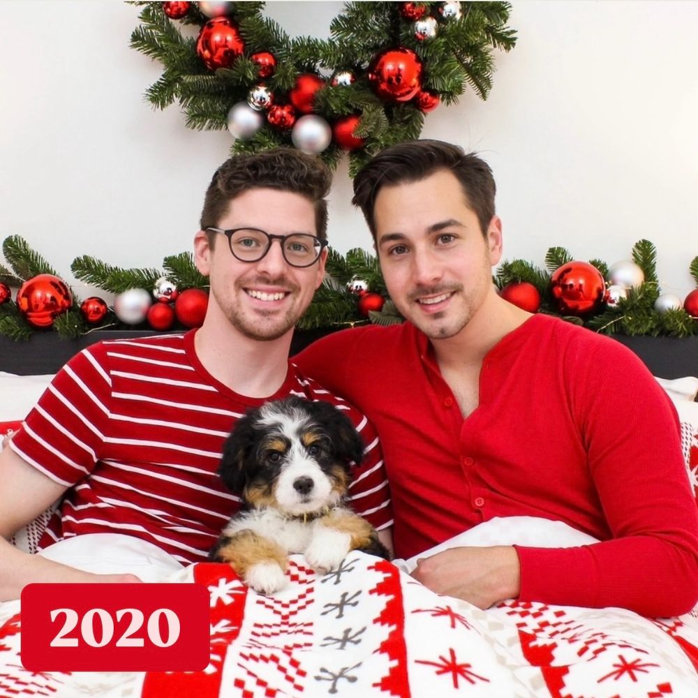 Two men posing in bed with a mini bernedoodle