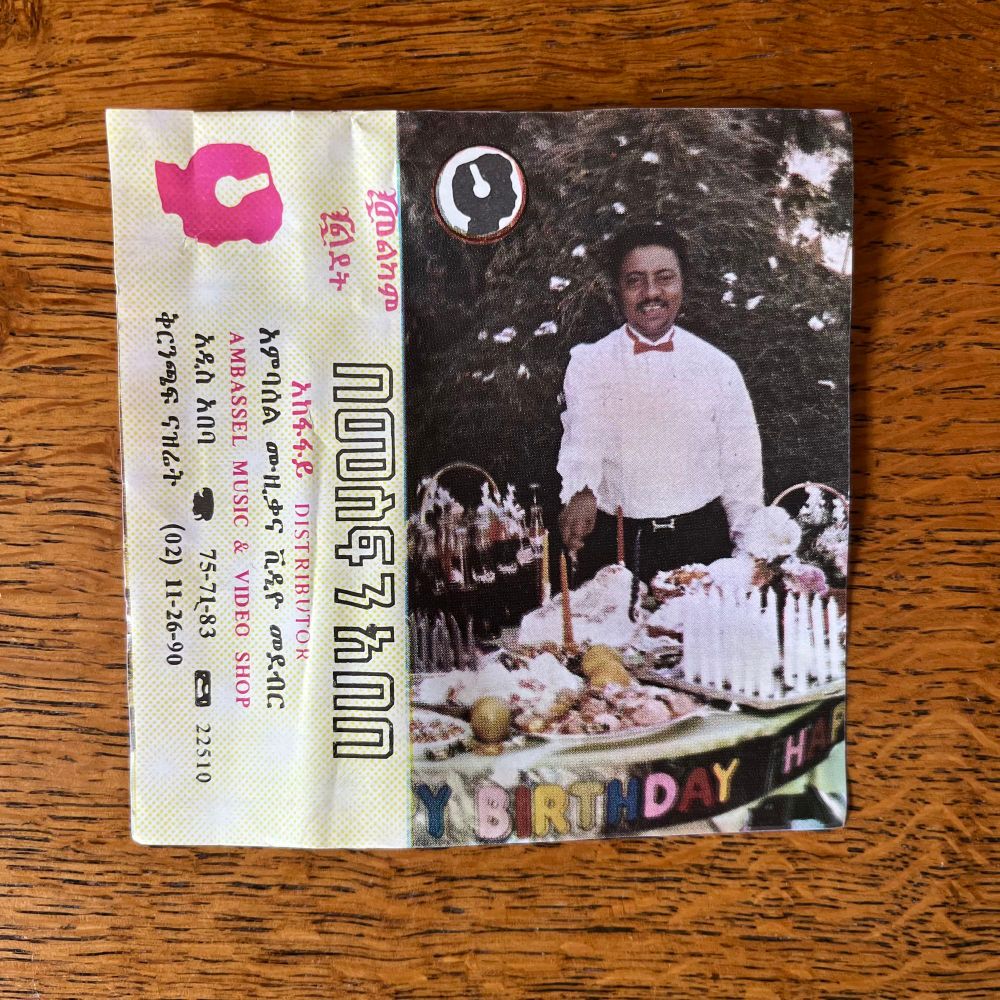 Ethiopian cassette inlay. A man stands behind a table which has a Happy Birthday banner pinned to it. 