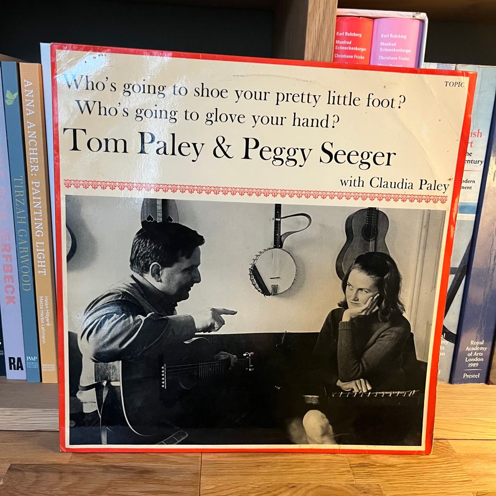 Tom Paley and Peggy Seeger. Who’s going to shoe your pretty little foot. The cover features a photograph of Tom and Peggy in conversation. Tom has a guitar on his knee and Peggy an autoharp, behind them we can see further instruments a guitar, a banjo and a dulcimer. 