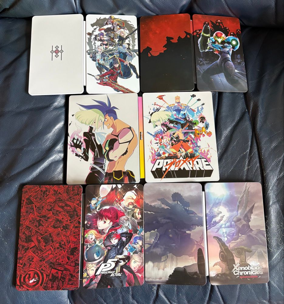 A photograph of a collection of 5 steelbooks laid open on a sofa. They are for (from top left) Xenoblade Chronicles 3, Metroid Dread, Promare, Persona 5 Royal and Xenoblade Chronicles Definitive Edition 