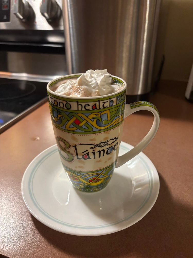 A mug with a Celtic theme and the words, “sláinte and good health” shows the chocolate foam and the whipped cream on top