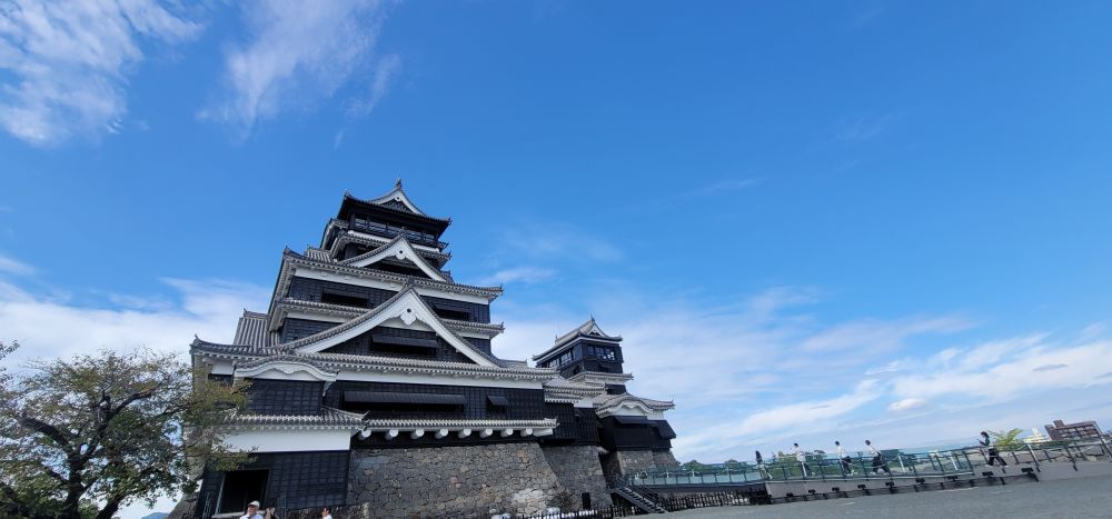A photo of Kumamoto Castle from below, set against a bright blue sky on a sunny day.