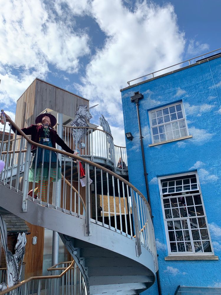 Blue sky and clouds in the sky and on the building of The Story Museum, Oxford - Story Guide standing looking up on the award -winning spiral staircase