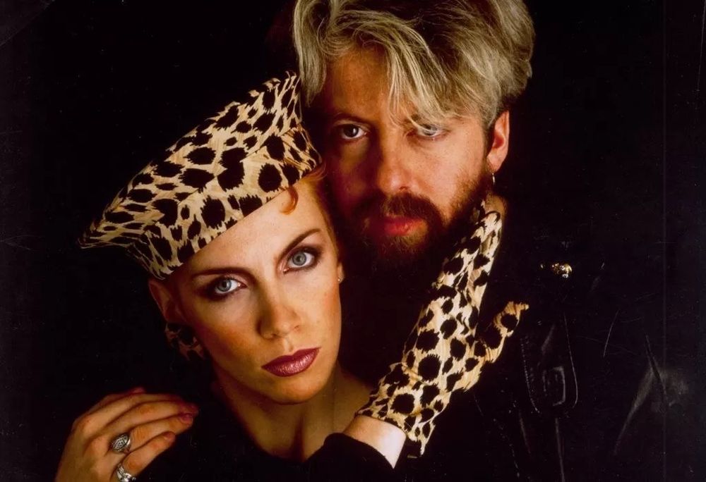 Eurythmics, which is Annie Lennox and Dave Stewart. Photo is circa _Touch_ era, with Annie wearing a leopard-skin hat and glove, and Dave with highlighted, poofy hair. 