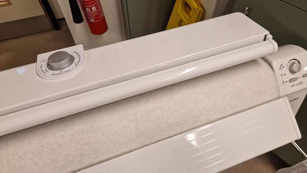 A white roller iron,  there is a dial in the top and a dial, buttons and indicator lights on the right hand side