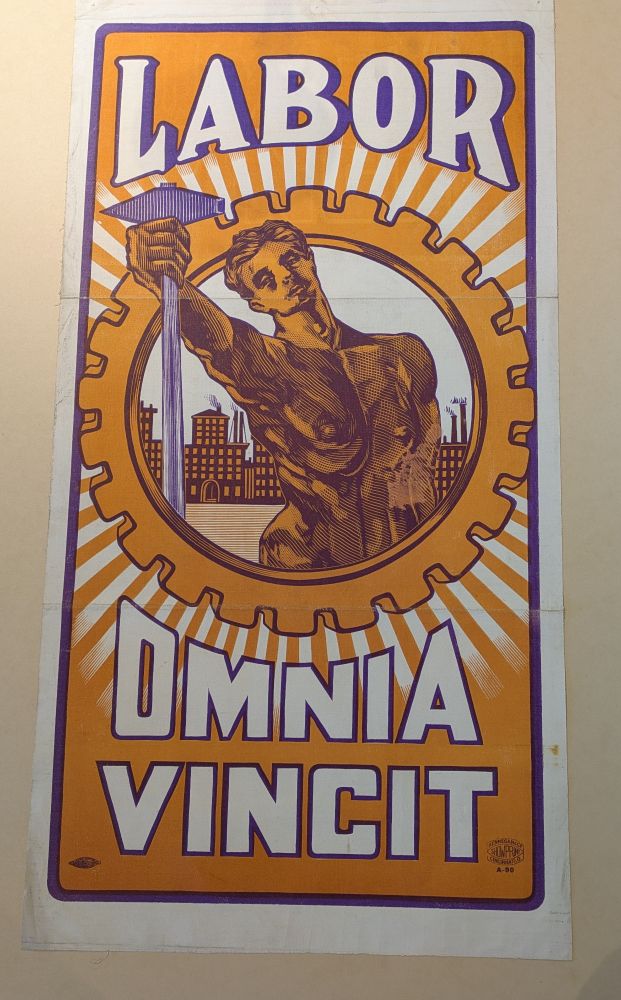 Printed poster, a laborer stands thrusting a hammer at the viewer. The words Labor Omnia Vincit surround them.