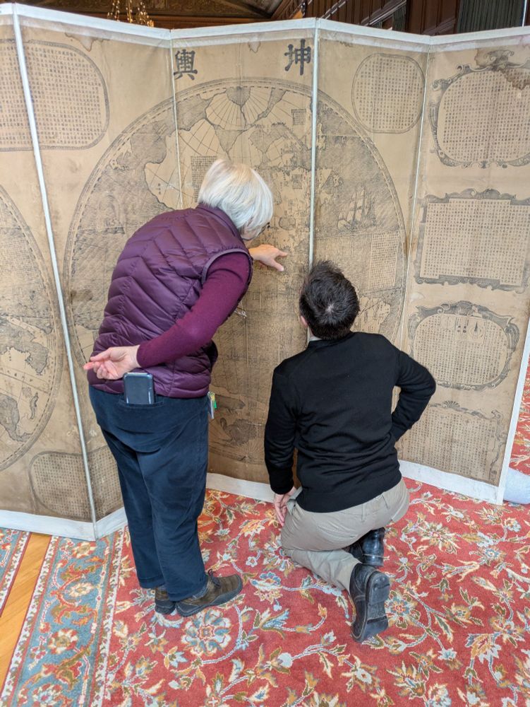 Two people in front of a double hemisphere map of the world.